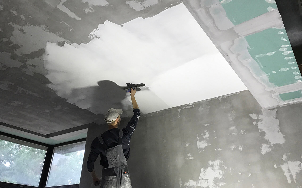 отделочник наносит шпатлёвку на оштукатуренный потолок